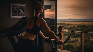 A woman exercising on a stationary bike with a scenic view of a landscape through a large window.