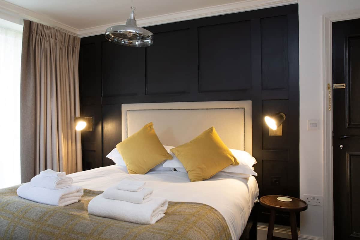 A hotel room with a large bed, two bedside lamps, a headboard, and a window with curtains.