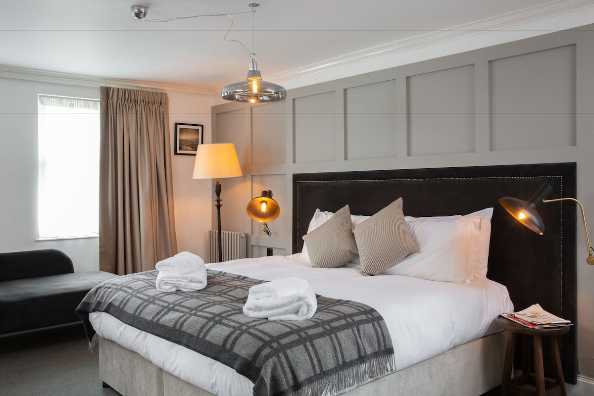A hotel room with a large bed, a desk, a chair, a lamp, and a window with curtains.