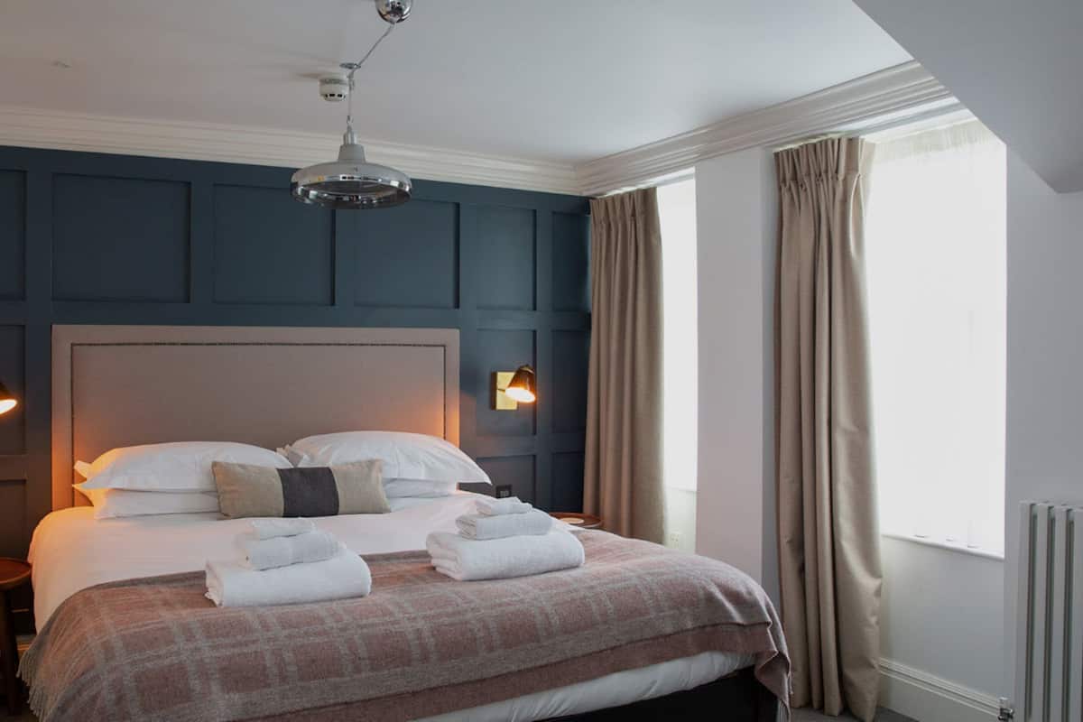 A neatly made bed with towels, a headboard, bedside lamps, and a window with curtains.