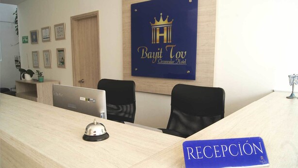 A hotel reception desk with a sign reading "RECEPCIÓN" and a sign above it for "Bayit Tov Circumvalar Hotel".