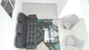 A modern living room with a black sofa, two armchairs, and a patterned rug.