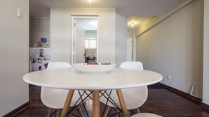 A dining area with a round table and four chairs, a kitchen in the background, and a hallway leading to another room. - InkaHuset Miraflores (Lima)