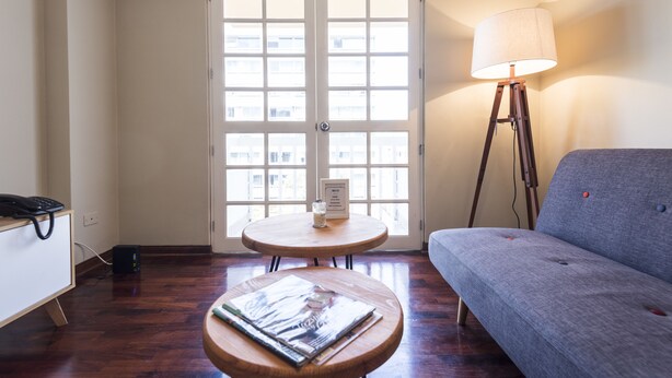 A room with a sofa, a round wooden table with a magazine, a lamp, and a desk with a phone. - InkaHuset Miraflores (Lima)
