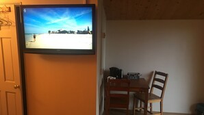 Una habitación con una televisión que muestra una escena de playa, una mesa de madera con sillas y una puerta.