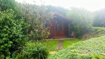 Una pequeña casa de madera roja rodeada de abundante follaje.