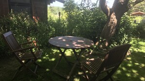 Una mesa de madera y dos sillas en un jardín, con un edificio de ladrillo al fondo.