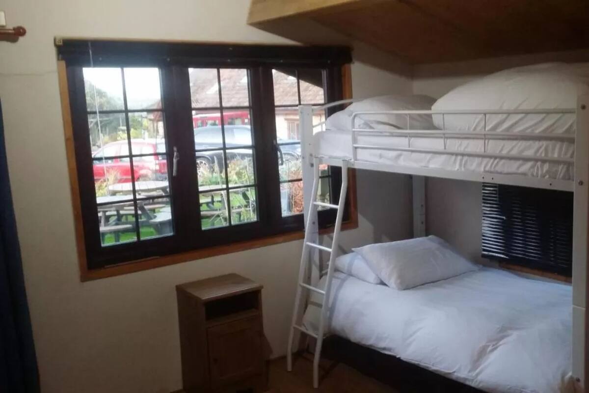 Dormitorio con literas, una ventana, un armario de madera pequeño y una escalera.