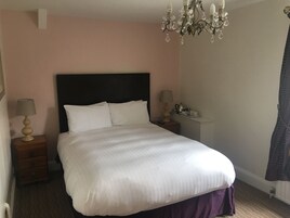 Una cama bien hecha con ropa blanca, cabecera oscura, mesitas de noche con lámparas y un candelabro.