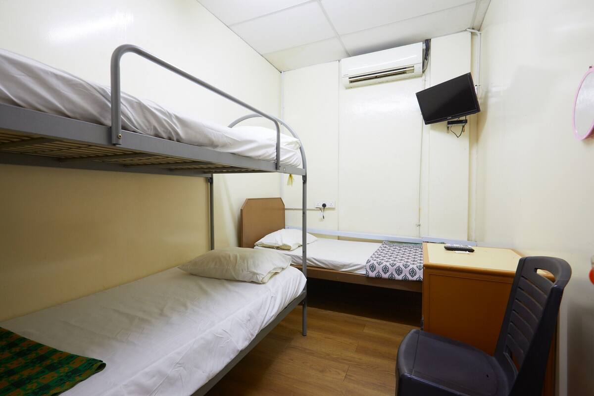 A bunk bed room with a desk and chair, a television, and an air conditioning unit.