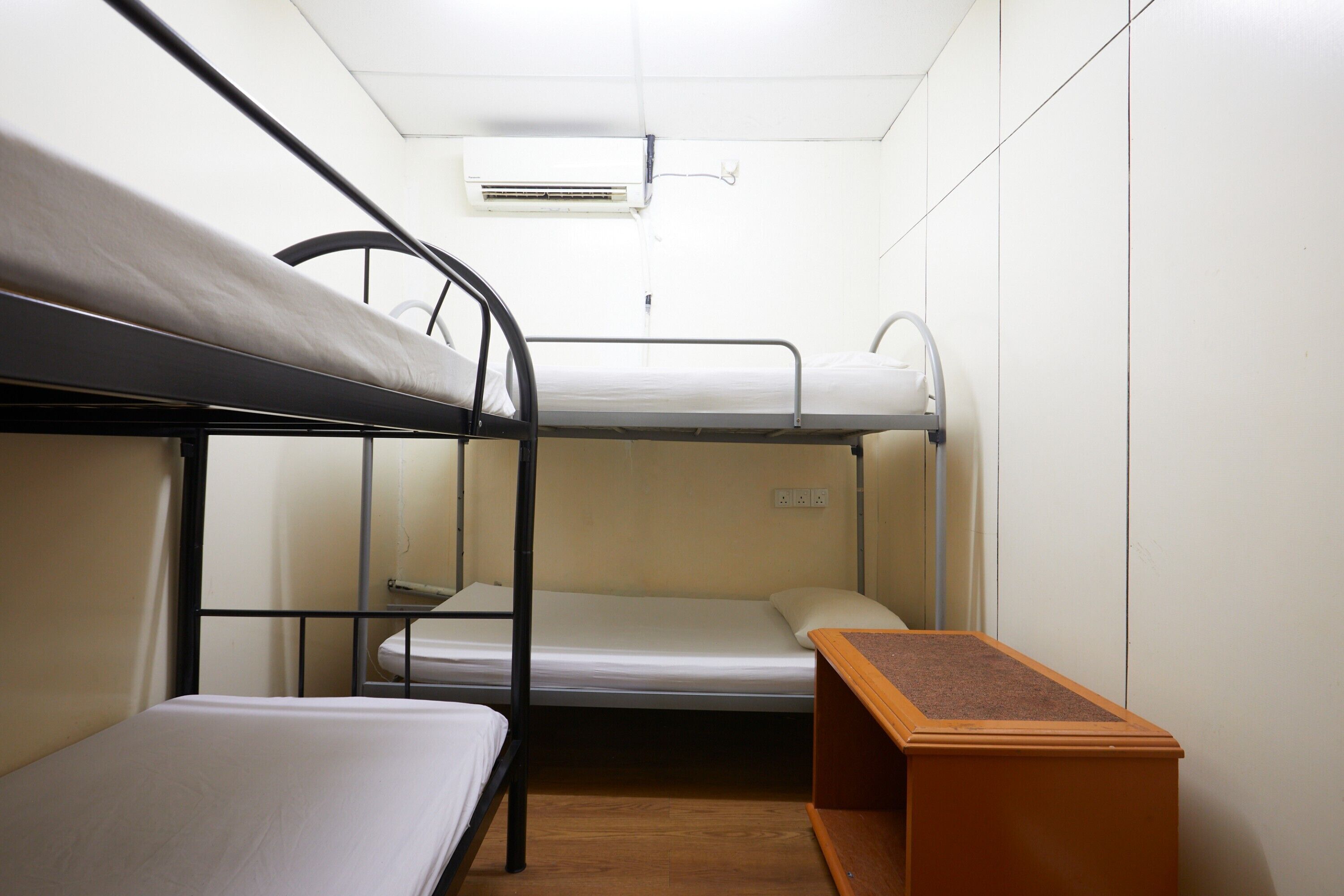 A bunk bed room with a wooden bench, a white air conditioner, and a white wall.