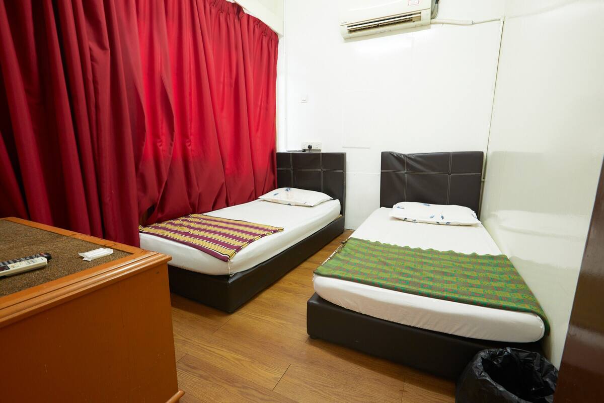 A hotel room with two single beds, a wooden dresser, a red curtain, and an air conditioning unit.