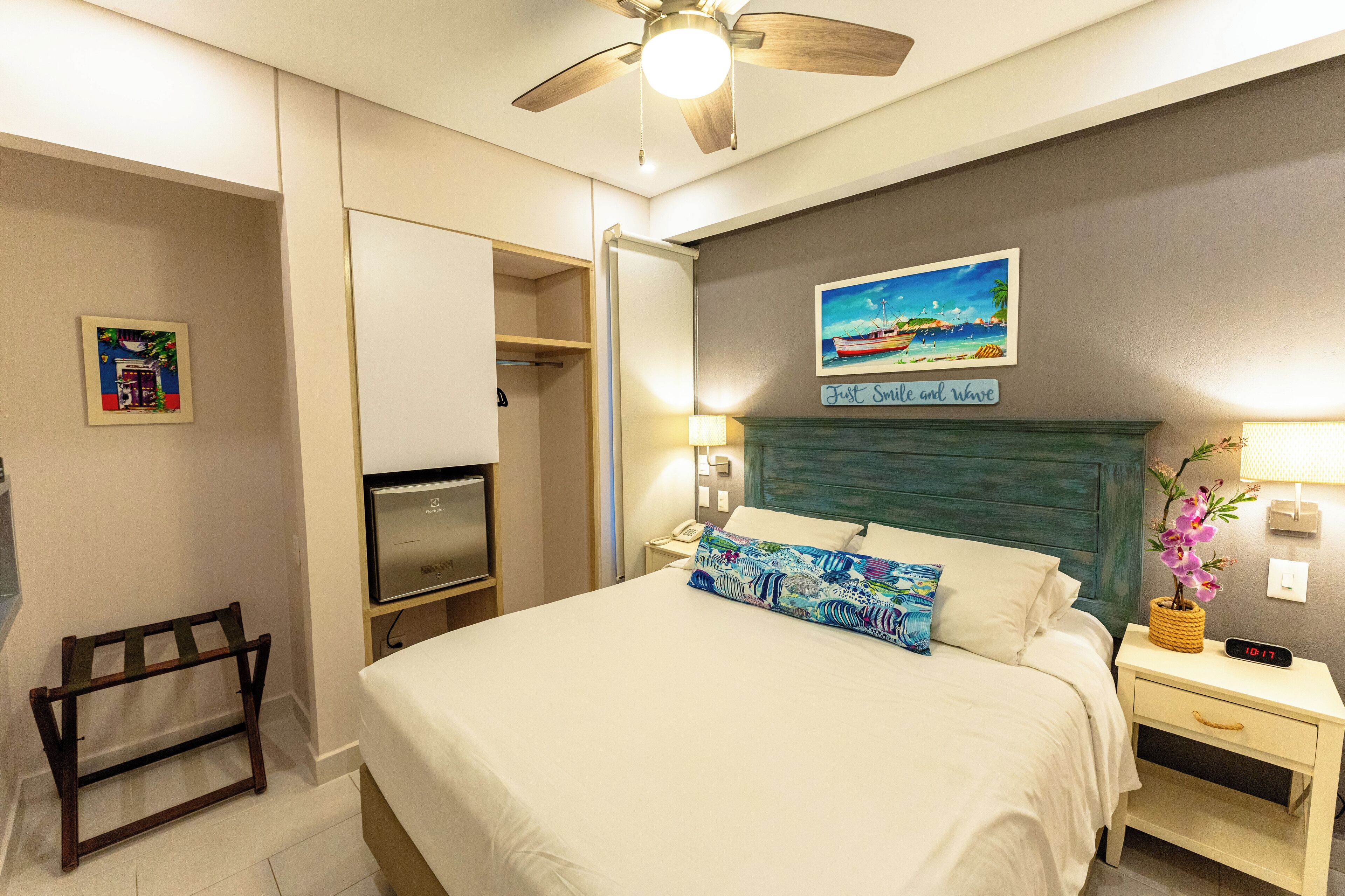 A hotel room with a bed, bedside table, nightstand, lamp, clock, and a ceiling fan.