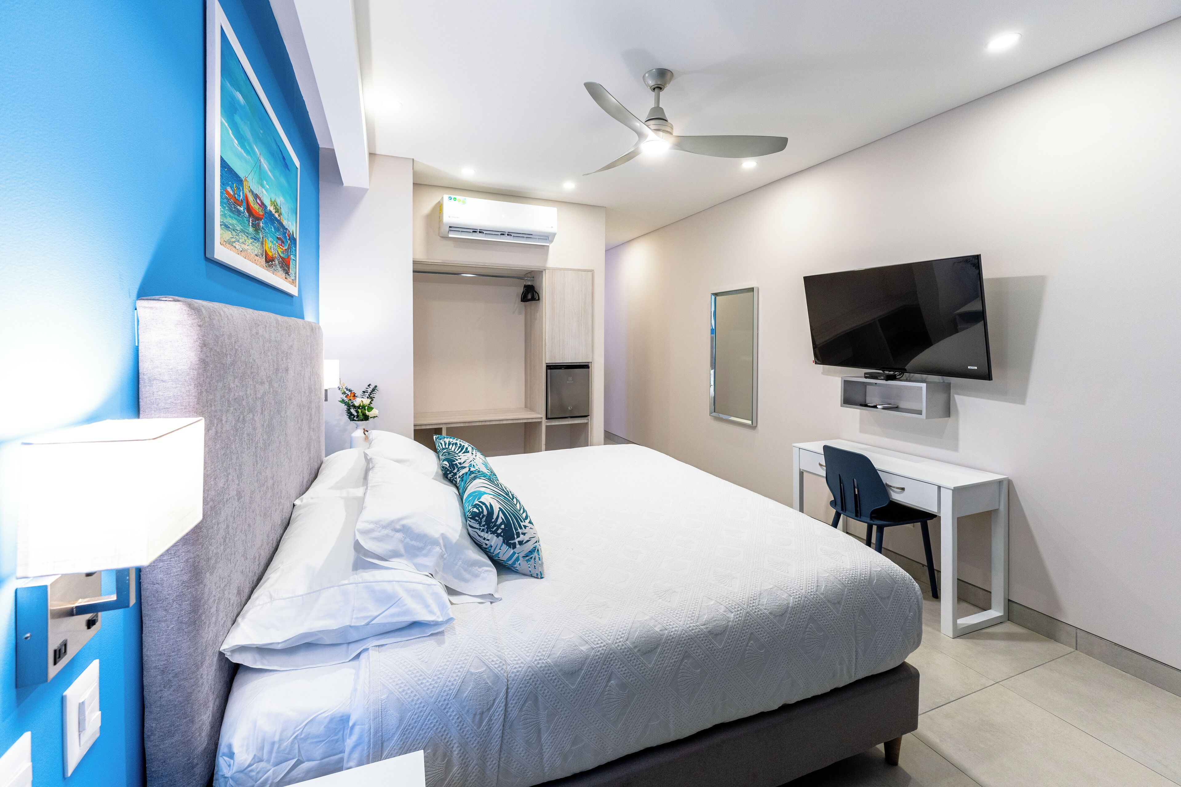 A modern hotel room with a large bed, a desk, a flat-screen TV, and a ceiling fan.