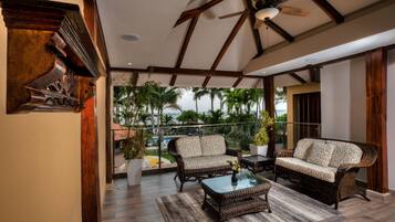 A spacious balcony with wicker furniture, a ceiling fan, and a view of palm trees.