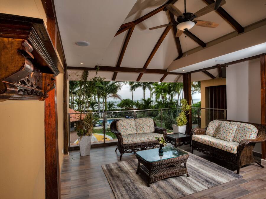 A spacious balcony with wicker furniture, a ceiling fan, and a view of palm trees.