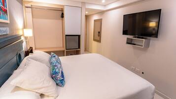 Habitación de hotel con cama, televisión montada en la pared, una puerta y un pequeño estante.