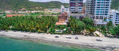 A coastal hotel with multiple floors, a beach, and palm trees.