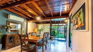 A dining area with a wooden table and chairs, a large window, and a painting on the wall.