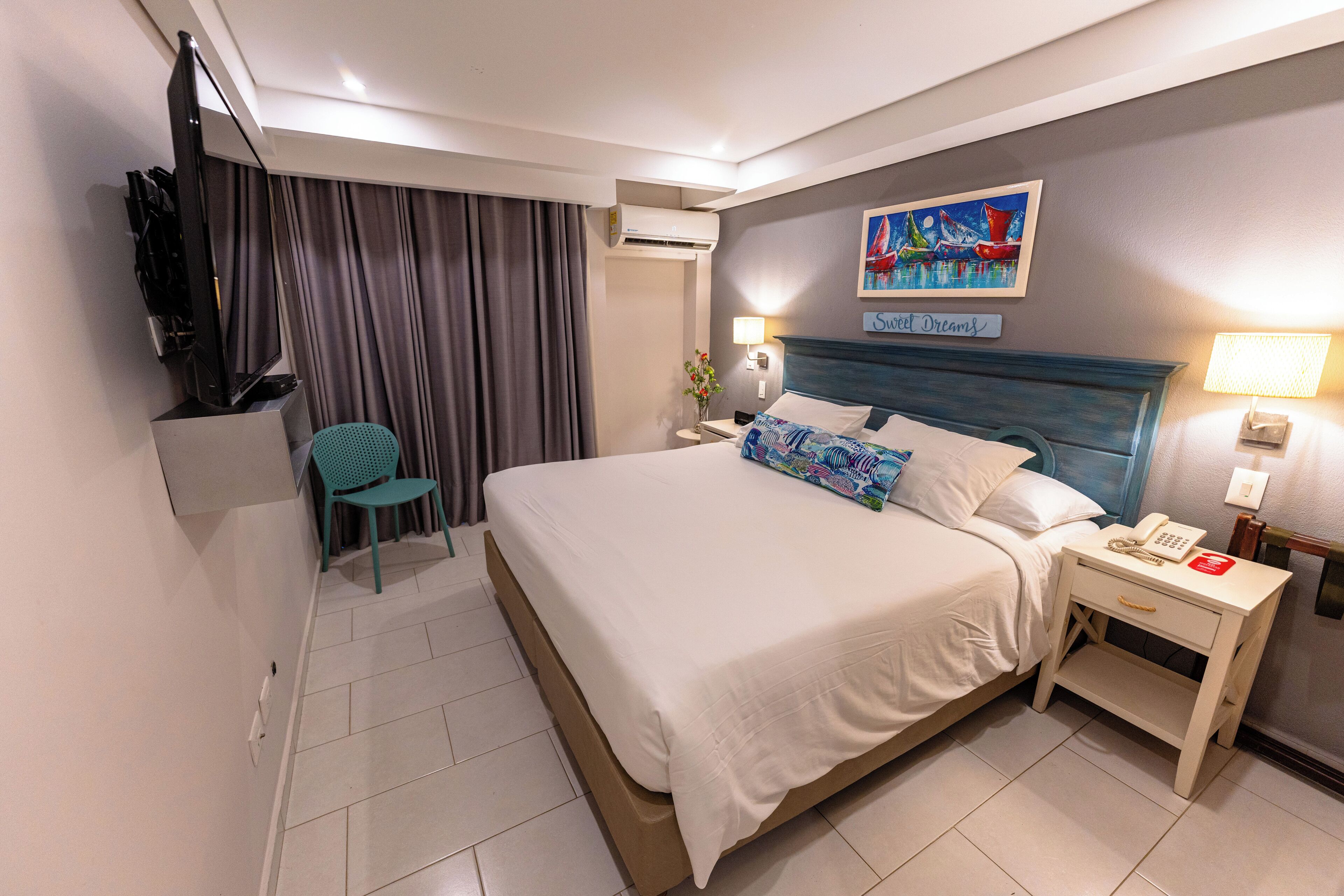 A hotel room with a bed, a desk with a telephone, a chair, a television, and a painting on the wall.