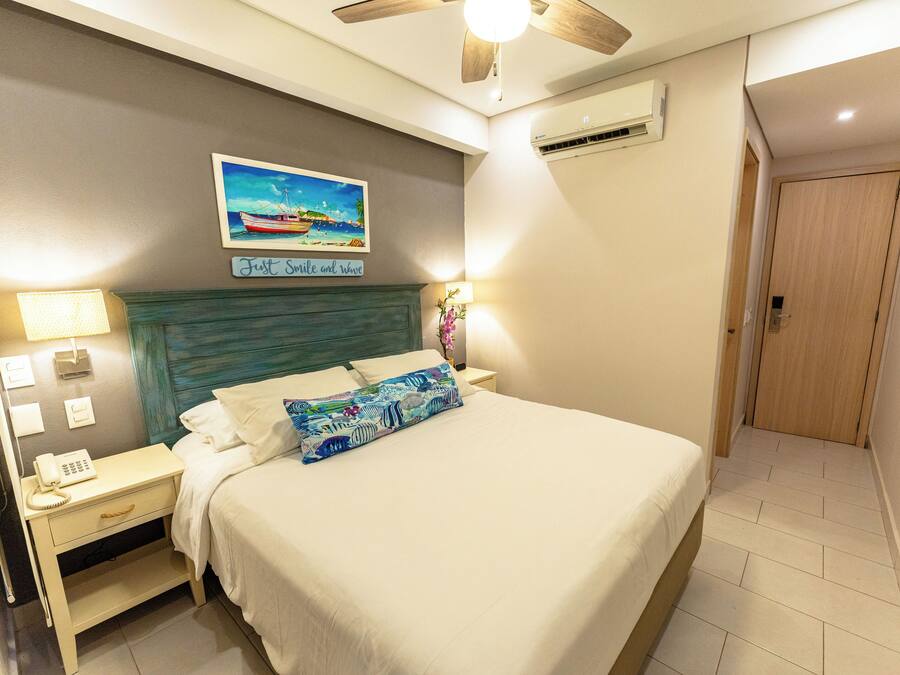 Een netjes ingerichte hotelkamer met een bed, nachtkastje, lamp en een schilderij aan de muur.