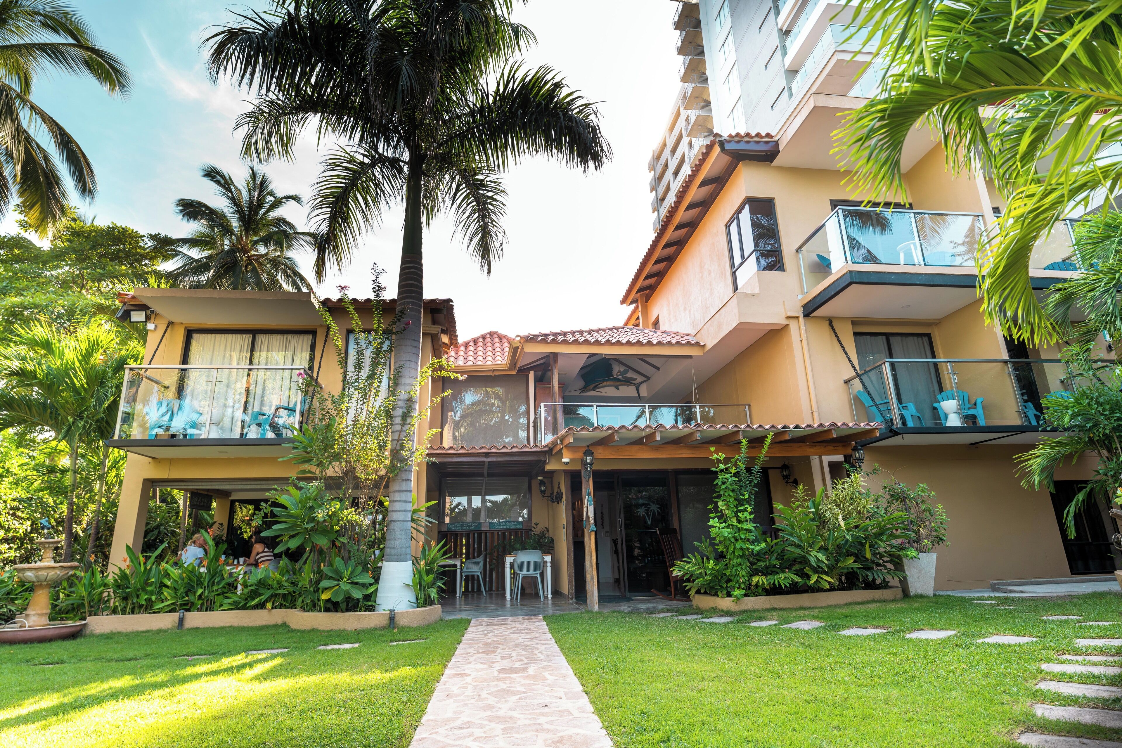 A multi-story hotel with a covered outdoor area, palm trees, and a pathway leading to the entrance.