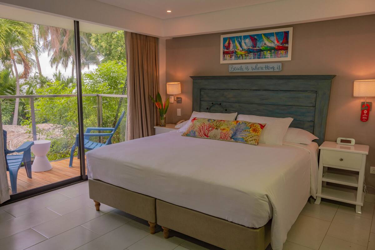 Une chambre avec un grand lit, une table de chevet, une commode, une fenêtre donnant sur un paysage verdoyant et un tableau accroché au mur.