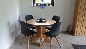 A round wooden table with four black chairs, a window above, and a tiled floor. - Ferienwohnung - Zoe (Sankt Wendel)