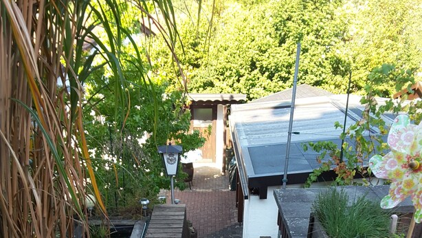 A narrow brick pathway leading to a building with a sloped roof, surrounded by greenery and a wooden fence. - Ferienwohnung - Zoe (Sankt Wendel)