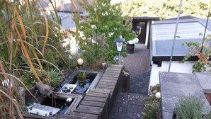 A wooden deck with a small pond, surrounded by plants and a brick pathway. - Ferienwohnung - Zoe (Sankt Wendel)