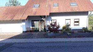 A two-story building with a red-tiled roof, a covered entrance, and a small garden area with potted plants. - Ferienwohnung - Zoe (Sankt Wendel)