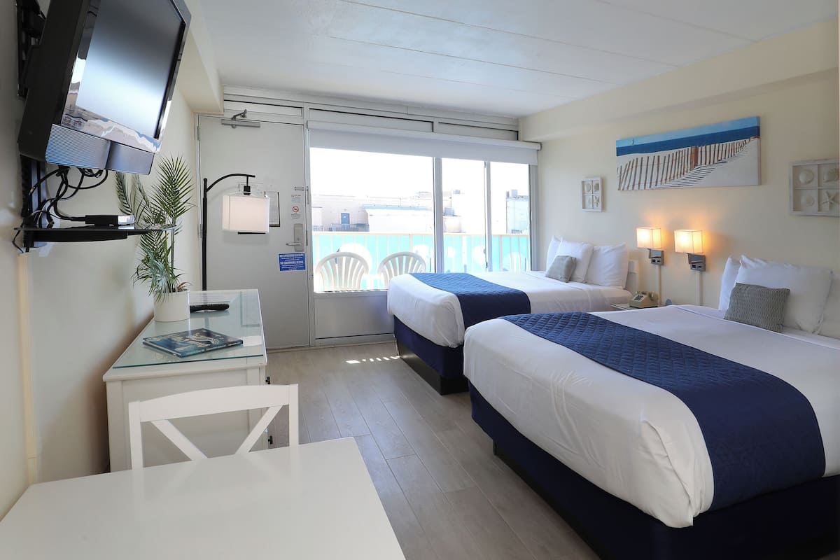 Habitación de hotel con dos camas, un escritorio, un televisor y un balcón con vistas.