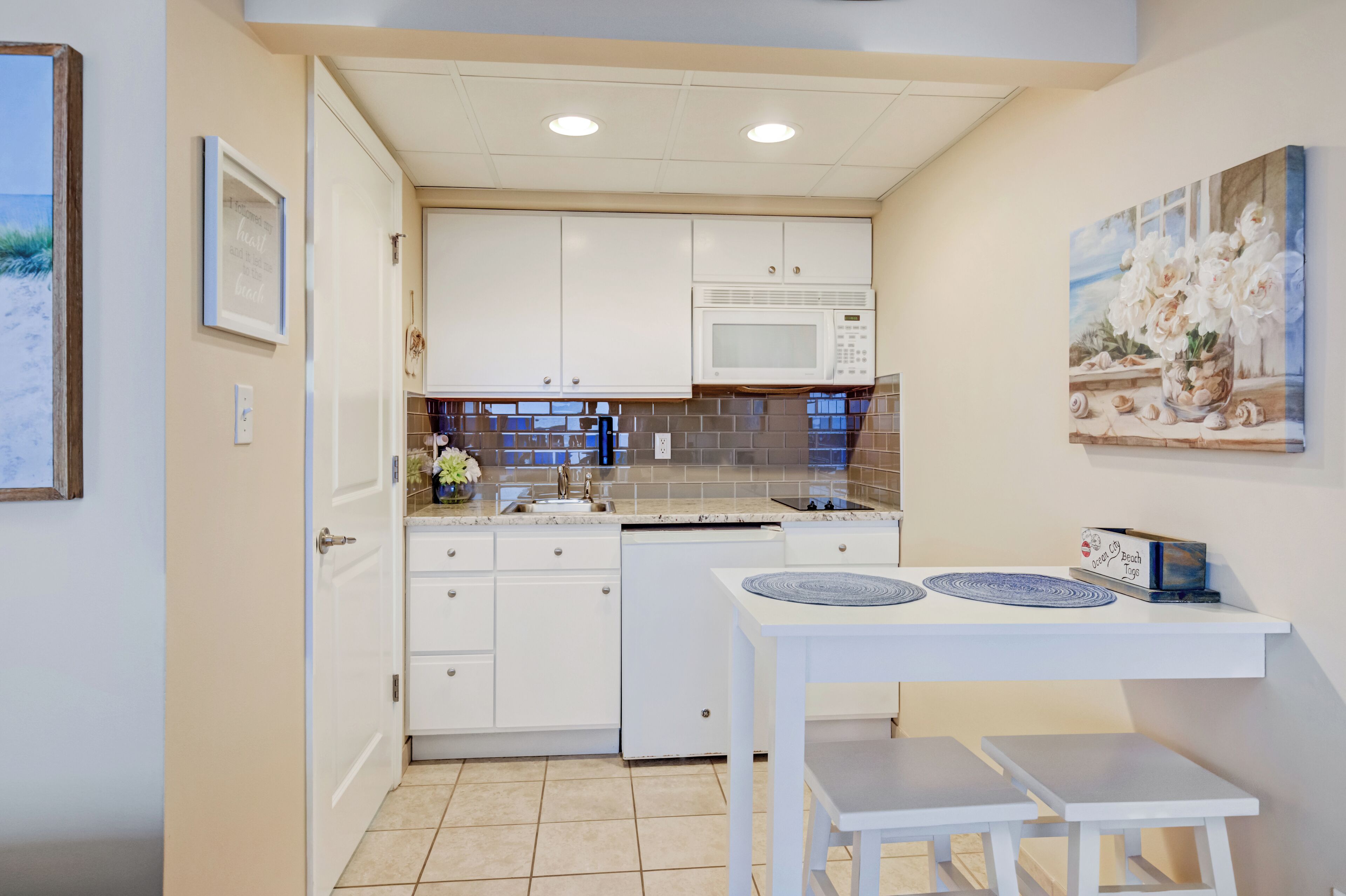 A compact kitchen with white cabinets, a microwave, and a small dining table with two chairs.