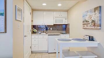A compact kitchen with white cabinets, a microwave, and a small dining table with two chairs.