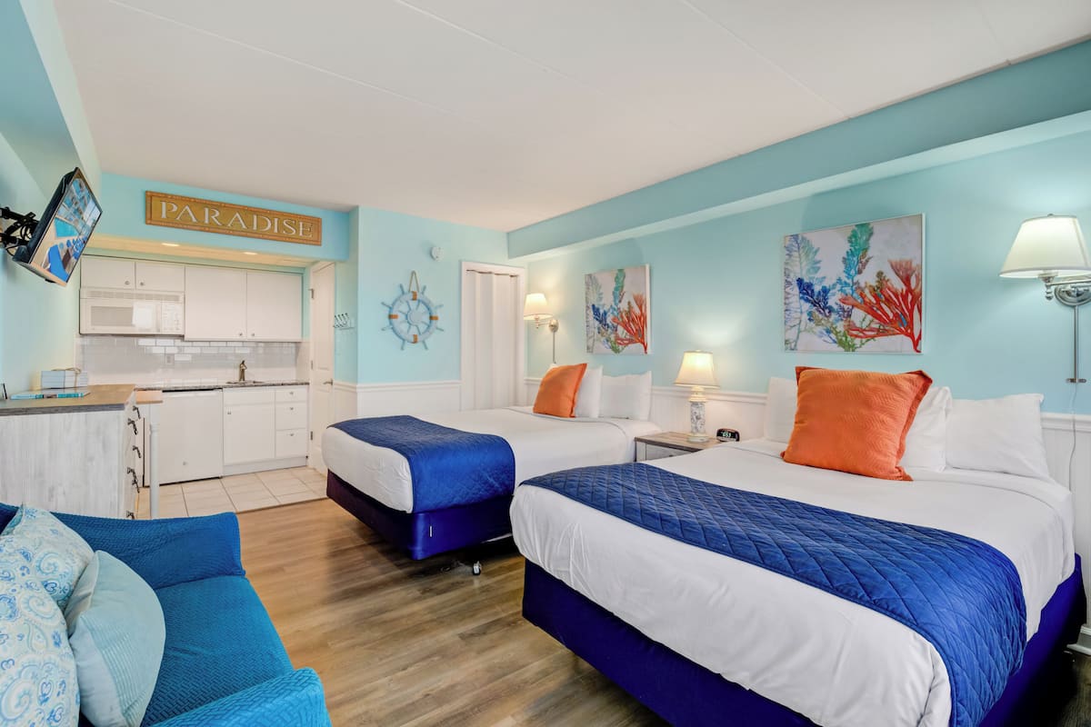 Una habitación de hotel con dos camas, una kitchenette, un sofá azul y obras de arte en las paredes.