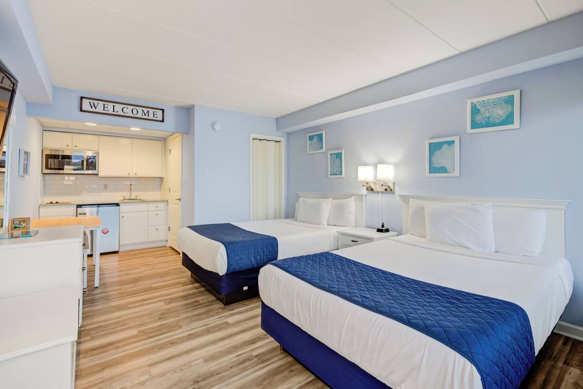 Habitación de hotel con dos camas, kitchenette y un cartel que dice 'WELCOME'.
