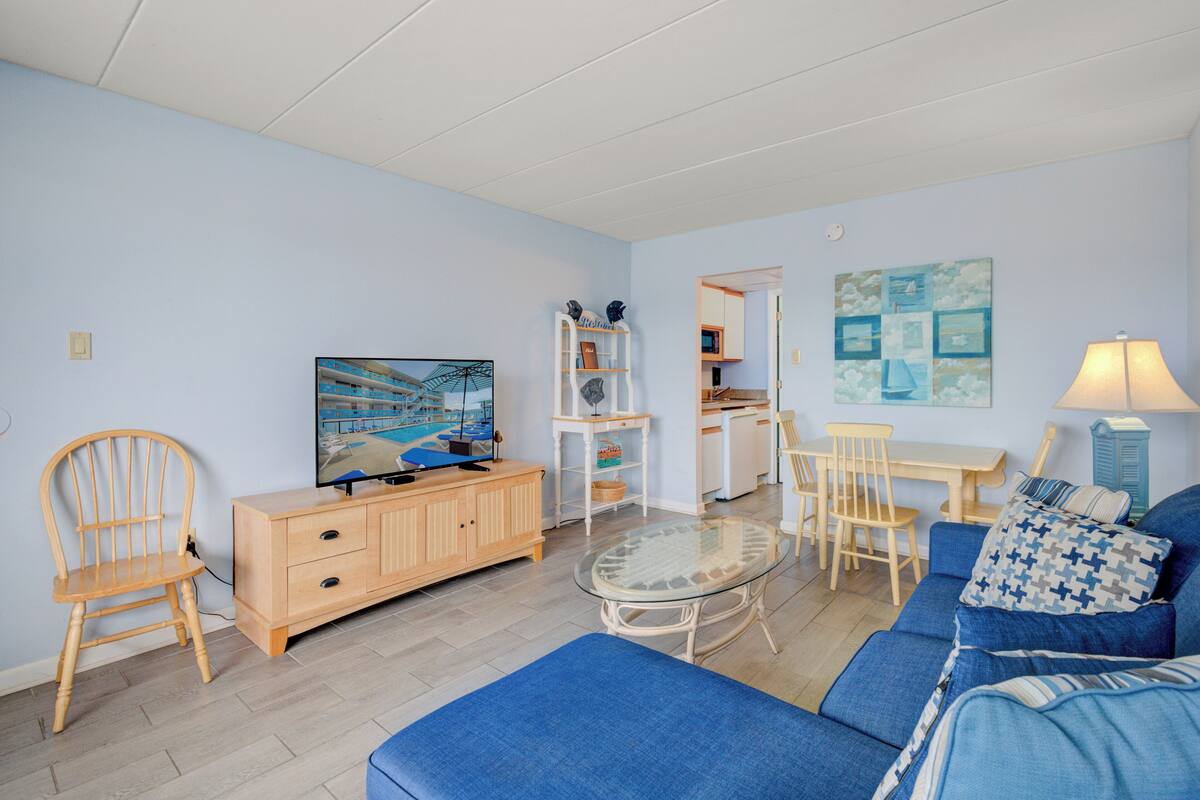 Una sala de estar con un sofá azul, un aparador de madera, una mesa de centro de vidrio y un televisor.