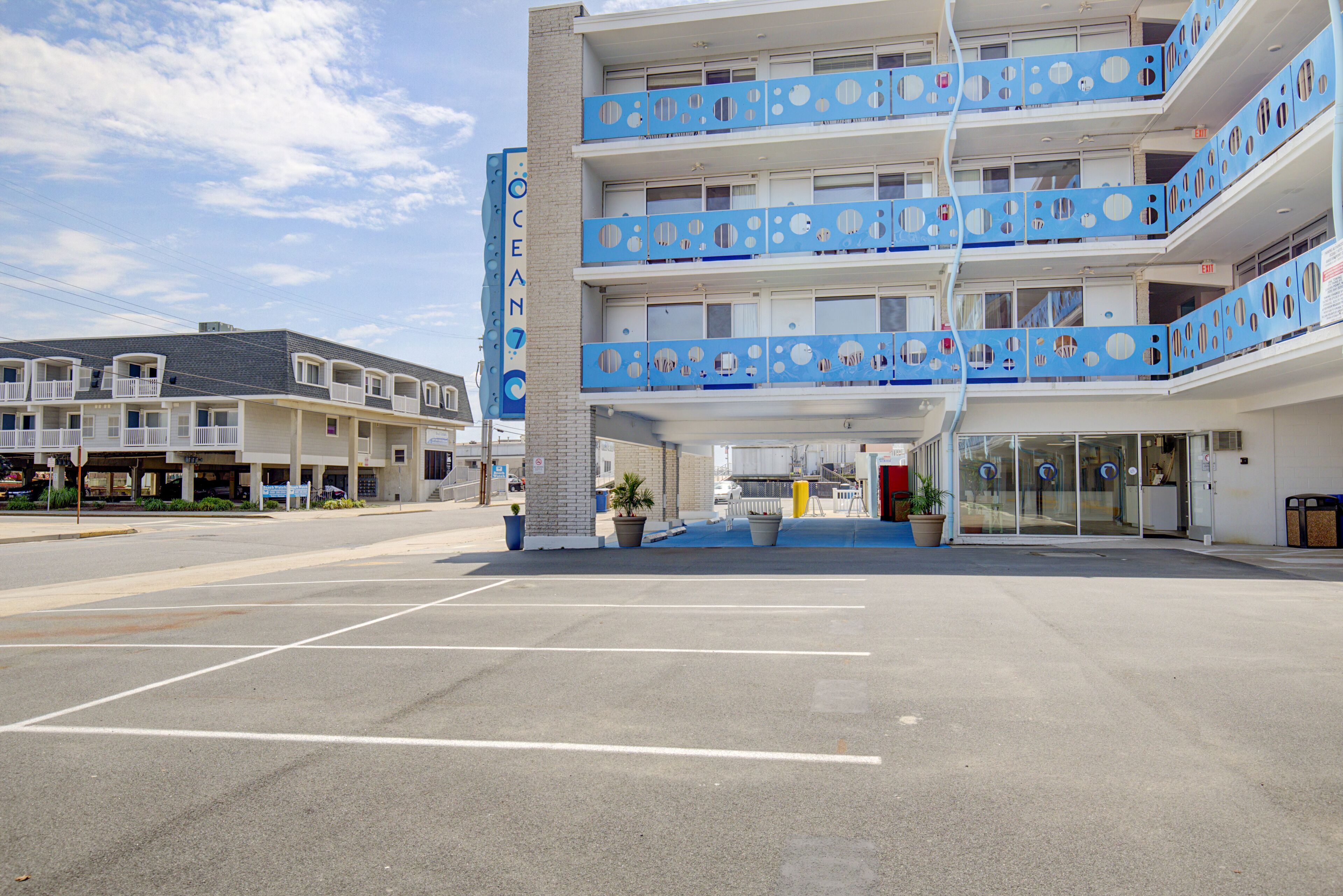 A multi-story hotel with balconies, a parking lot, and a clear sky.