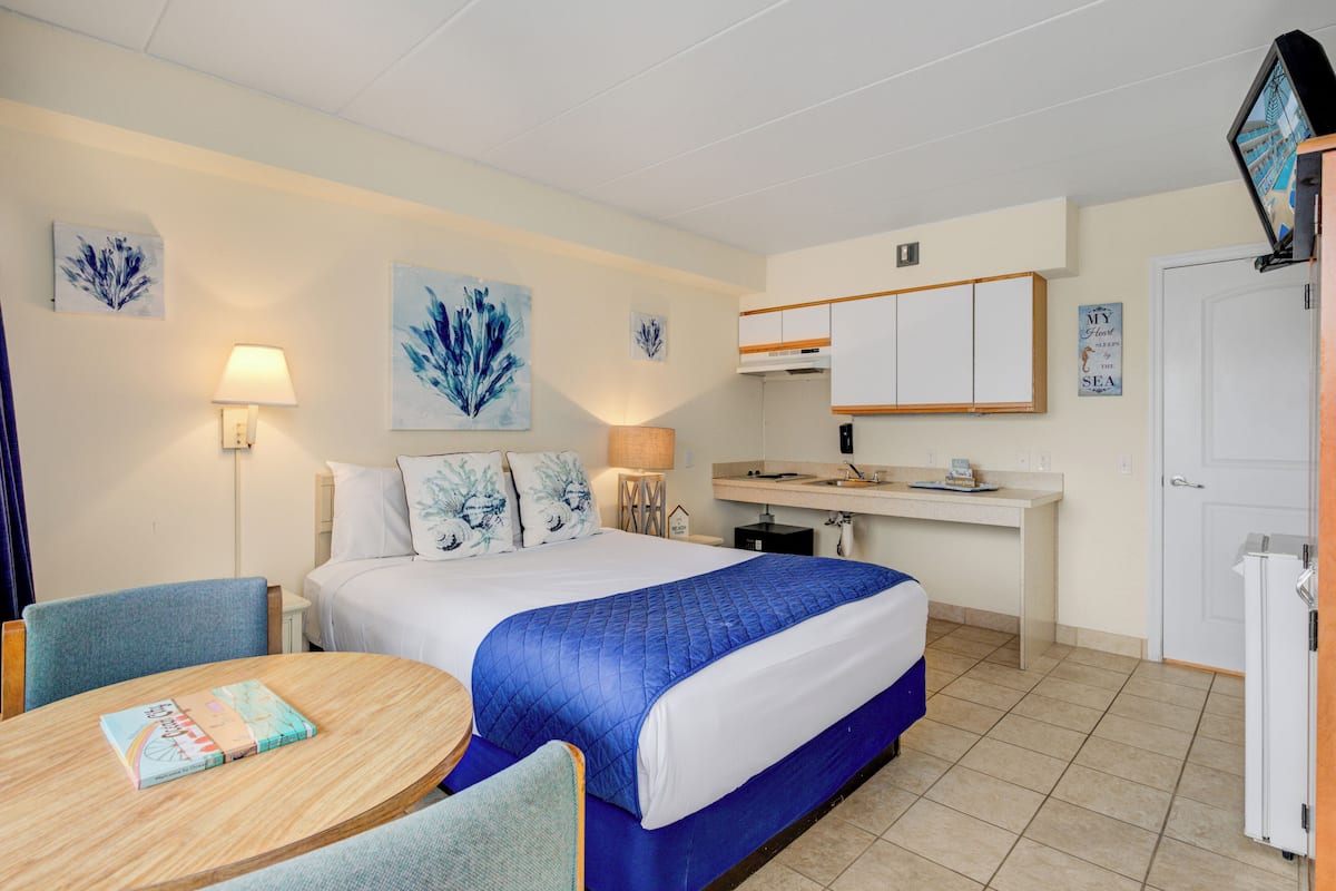 Una habitación de hotel con cama, escritorio, silla, lámpara y obras de arte en las paredes.