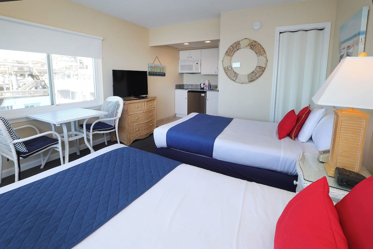 Habitación de hotel con dos camas, un escritorio, televisor, kitchenette y vistas a la ciudad.