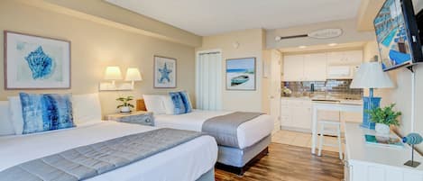 A hotel room with two beds, a desk, and a kitchenette.