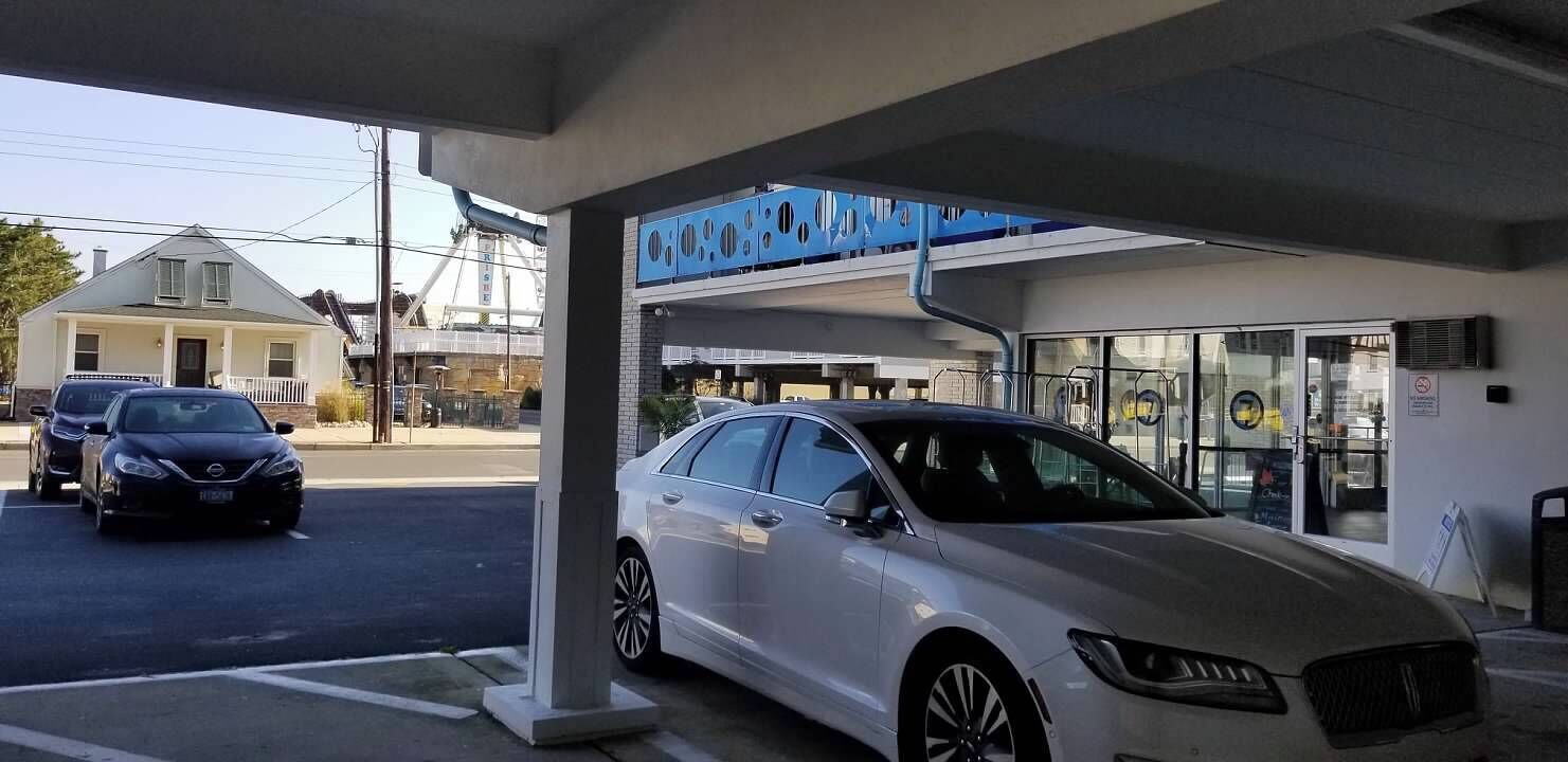 A gas station with a white car parked inside, a blue sign above the entrance, and a building with a glass facade in the background.