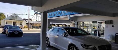 A gas station with a white car parked inside, a blue sign above the entrance, and a building with a glass facade in the background.