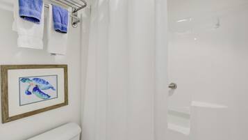 A bathroom with a white toilet, a framed picture of a sea turtle, and two towels hanging on a rack.