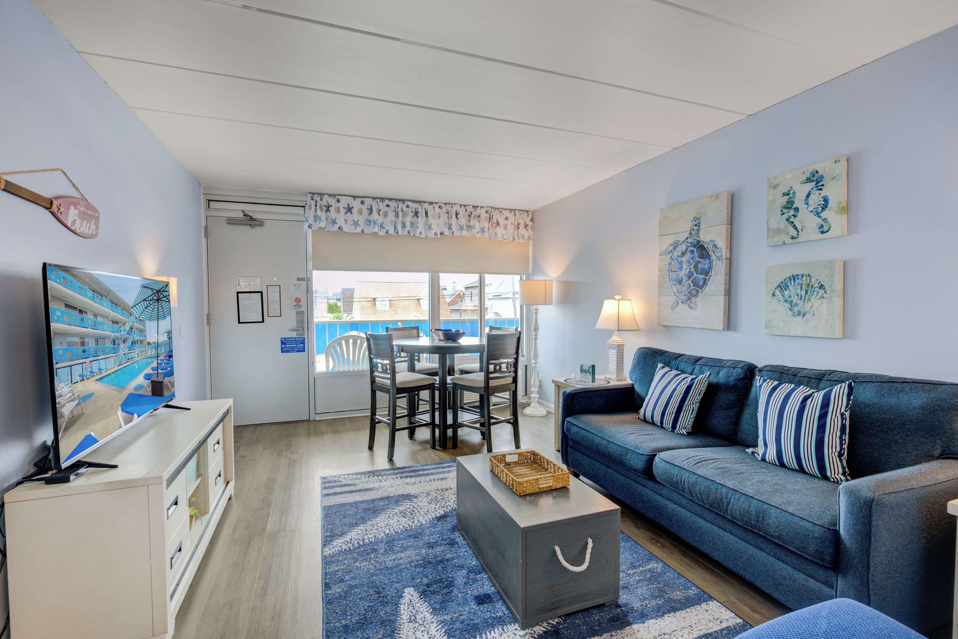 A living room with a blue sofa, a coffee table, a TV, and a dining area with chairs and a table.