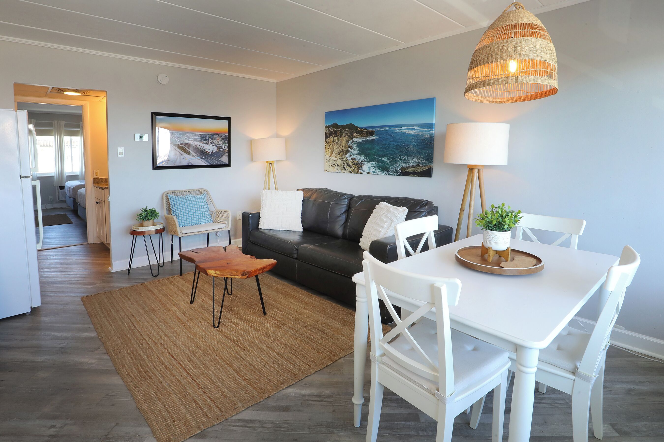 Un salon moderne comprenant un canapé, une table à manger, des chaises, une lampe et un grand tableau représentant un paysage côtier.