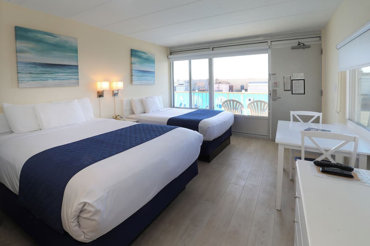 Una habitación de hotel con dos camas, un escritorio y vista al mar.