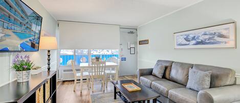A living room with a sofa, a coffee table, a TV, and a dining area with chairs and a table.