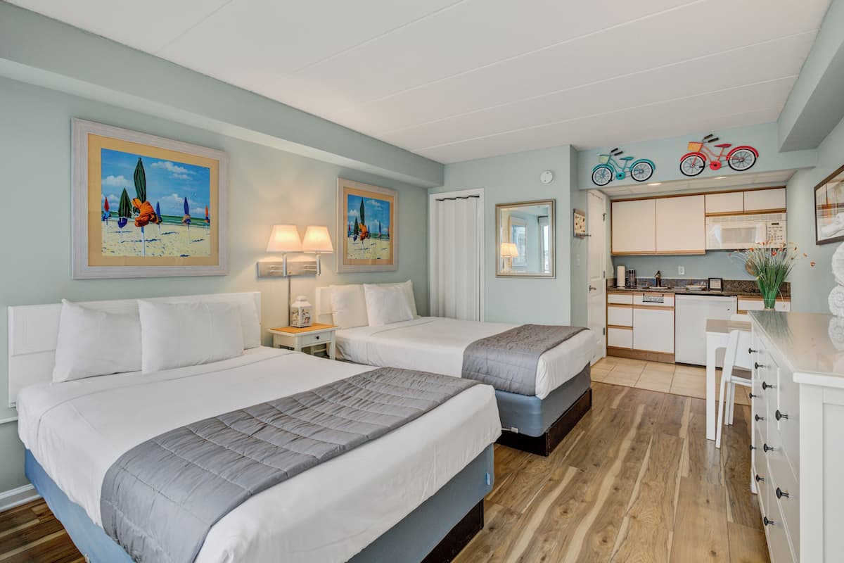 Habitación de hotel con dos camas, una kitchenette pequeña y un baño con cortina de ducha.