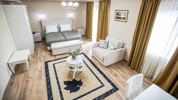 A modern bedroom with a large bed, bedside tables, a sofa, and a small table with a vase. - Hotel Borova (Korçë)